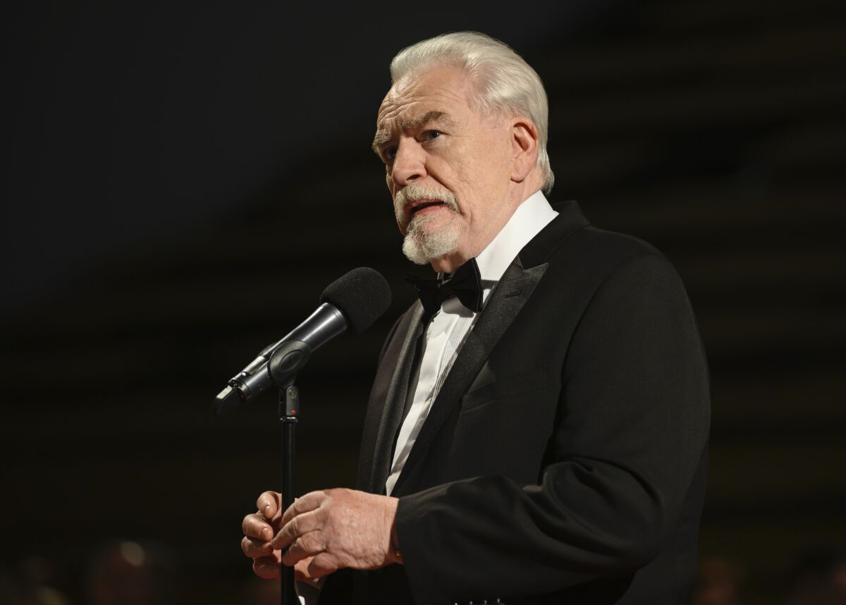 A silver-haired gentleman in a dark tuxedo at a microphone.