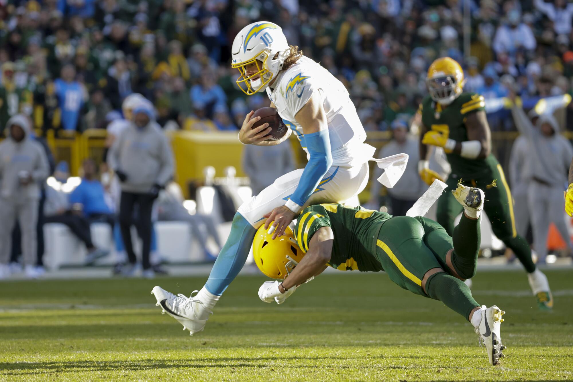 Chargers quarterback Justin Herbert runs with the ball as Packers safety Anthony Johnson Jr. tries to bring him down.