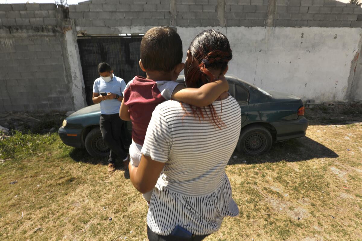 A man leans against a car while a woman holds a small child.