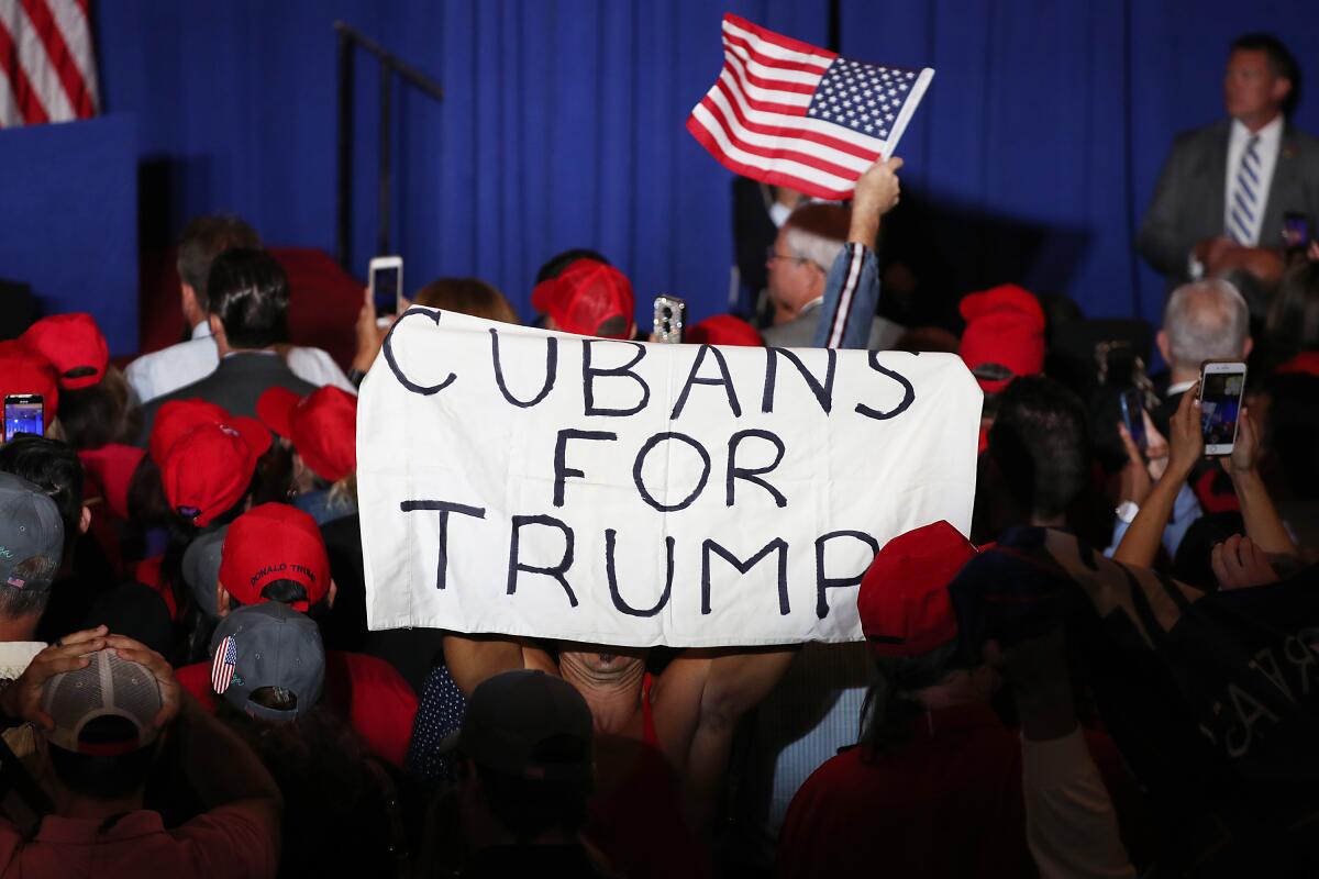 A crowd of people in red baseball caps with a sign that says "Cubans for Trump"