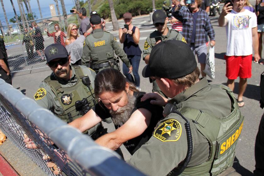 With sheriff's deputies holding him in place, Alan Hostetter clings to a fence at the Pier Bowl parking lot on May 21, 2020, as part of a rally he organized to demonstrate against the fencing around the lot.