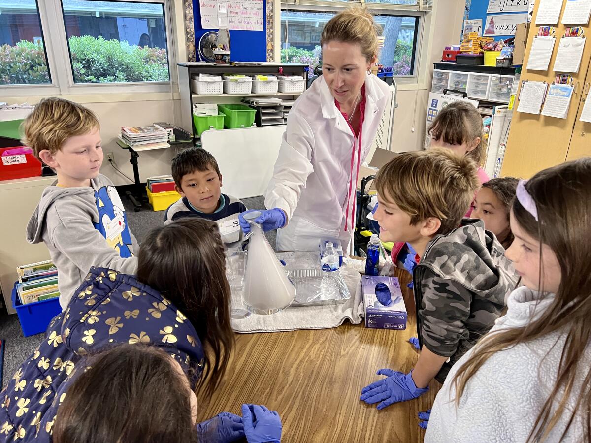 A woman in a lab coat demonstrates dry ice before children