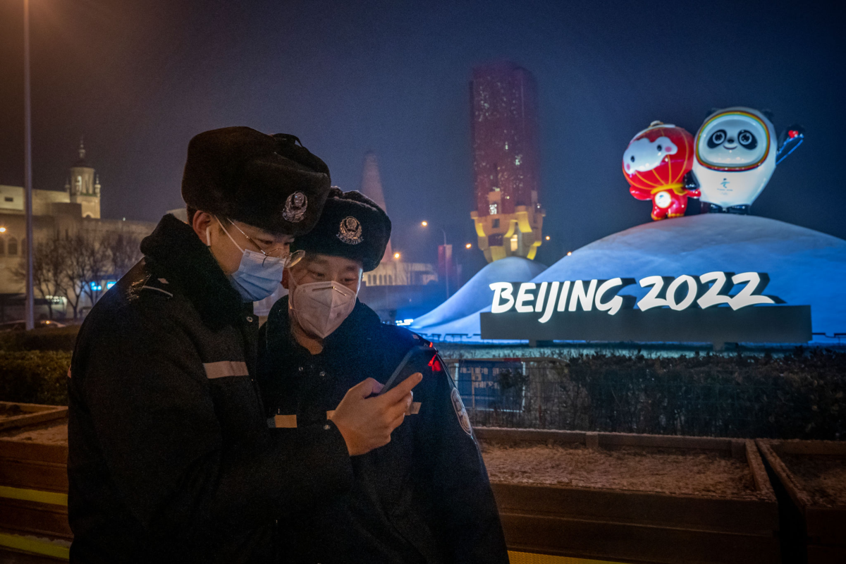 Two policemen look at a phone in front of a Beijing 2022 sign