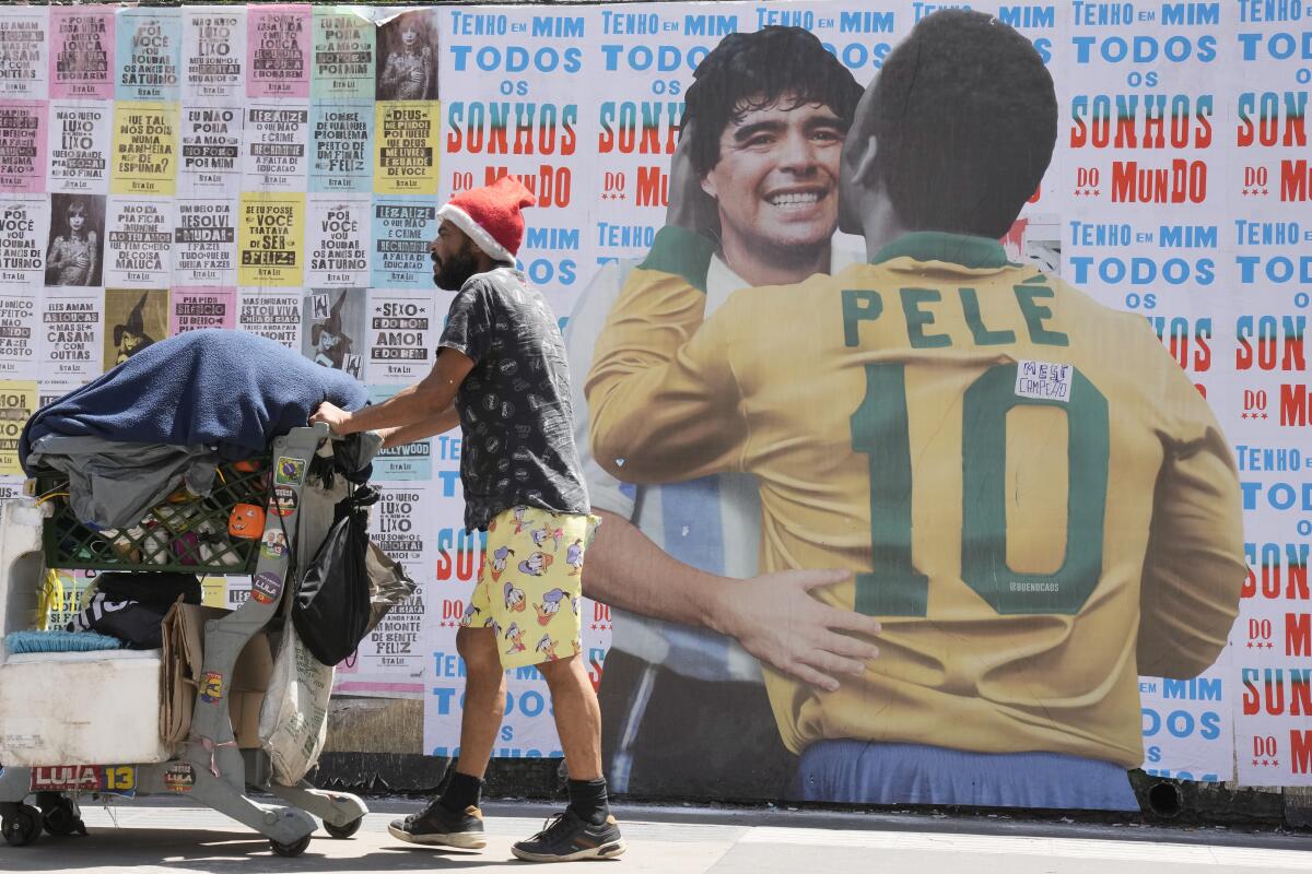 A man pushes a cart loaded with items for recycling in front of a mural of Pele embracing the late Diego Maradona.