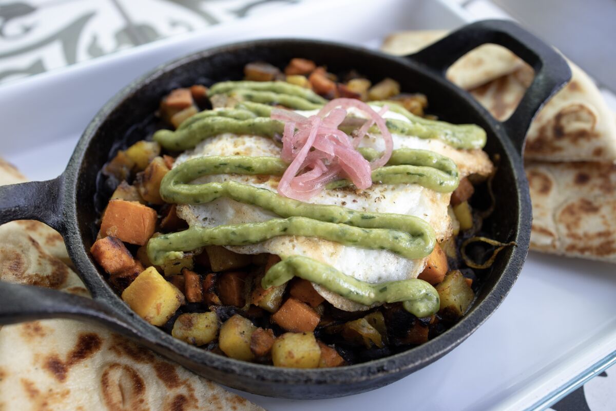 The Medina Breakfast Skillet is served in a cast iron pan with cubed sweet potatoes, black beans, caramelized onions, merguez sausage and topped with a fried egg and roasted jalapeno-avocado salsa.