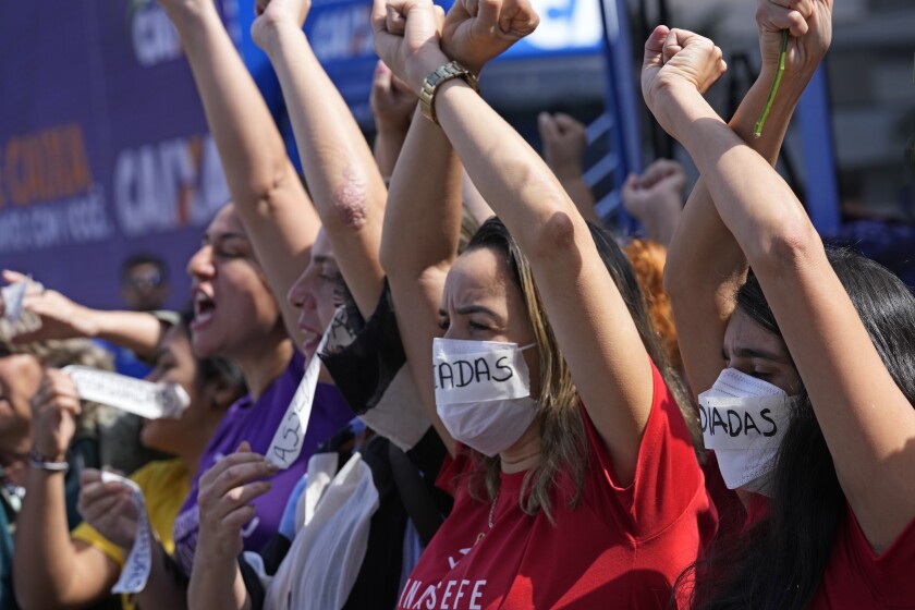Employees of Caixa Economica Federal bank raise their arms and wear stickers over their mouths, that read "Harassment" in Portuguese, to protest the president of the institution Pedro Guimaraes after allegations of sexual harassment, outside the bank's headquarters in Brasilia, Brazil, Wednesday, June 29, 2022. (AP Photo/Eraldo Peres)