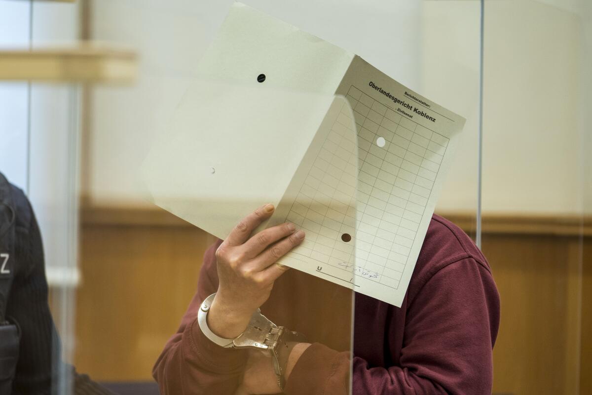 A man in a courtroom holds paper over his face.
