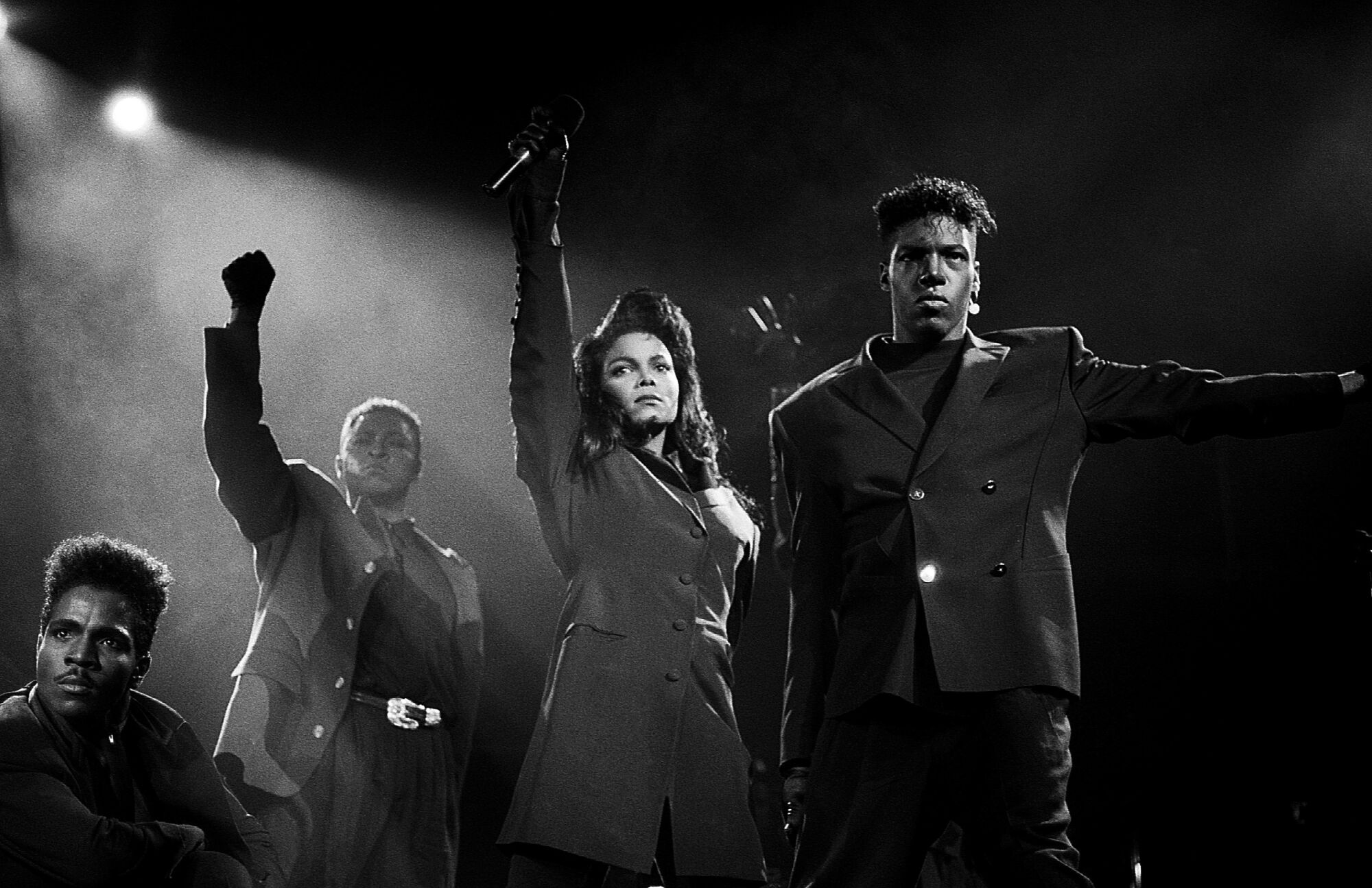 Black-and-white photo of Janet Jackson raising her fist, flanked by three performers, one of whom is raising his fist 