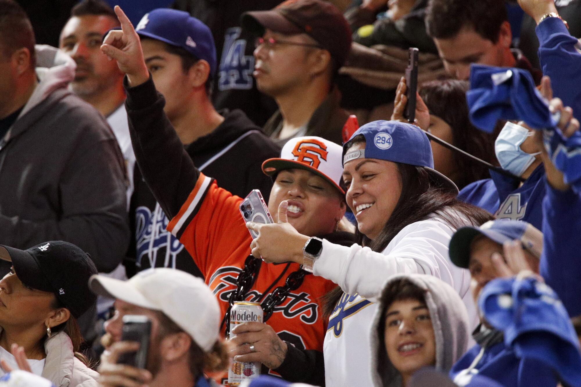 A San Francisco Giants looks at a phone with a Los Angeles Dodgers fan in the stands