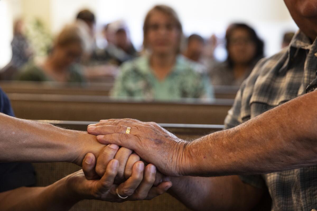 Jose Salomon, left, and Ruben Valencia, right, hold hands during a during a memorial service for Raul Guerra.(Dania Maxwell / Los Angeles Times)