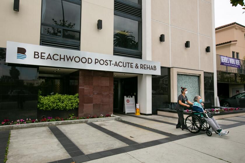 SANTA MONICA, CA - APRIL 13: A worker escorts a resident out of Beachwood Post-Acute in Santa Monica during the coronavirus pandemic on Monday, April 13, 2020 in Santa Monica, {state. This facility ranks among the top in Los Angeles cited for poor infection control in the last three years. ({photographer} / Los Angeles Times)