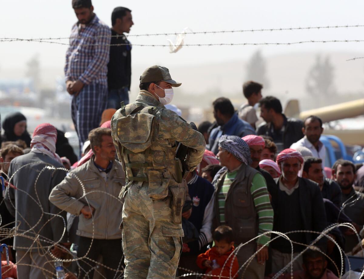 A Turkish soldier stands as Syrians from the town of Kobani wait to enter Turkey at the Yumurtalik border crossing Oct. 2.