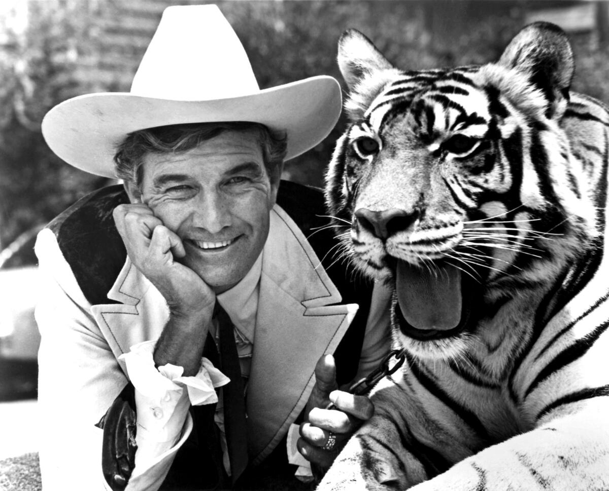 A man in a cowboy hat rests his chin on his hand while posing with a tiger