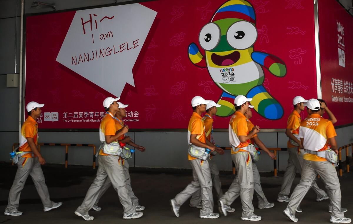 Volunteers walk past a poster introducing the official mascot of the 2014 Youth Olympic Games as competition gets underway on Aug. 15 in Nanjing, China.