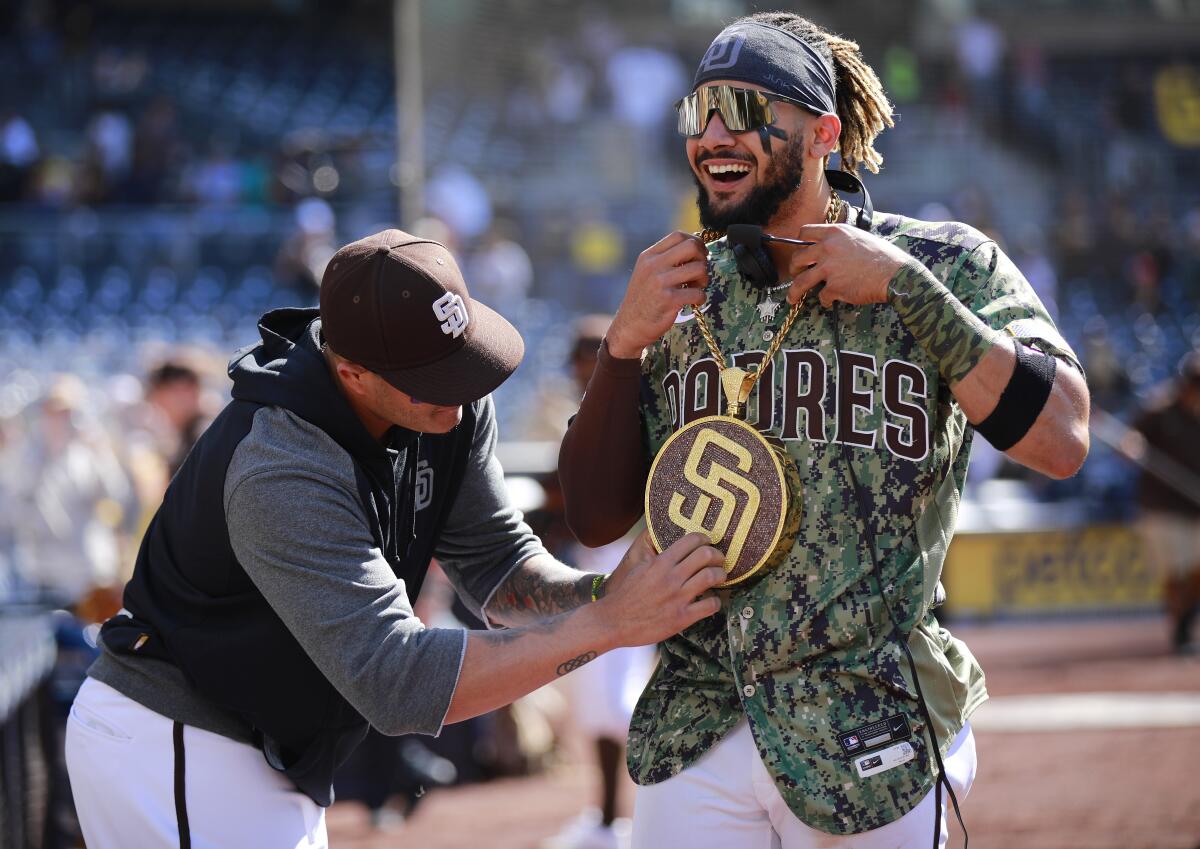Manny Machado puts the Padres' new 'Swagg Chain' on Fernando Tatis Jr. after Sunday's 9-2 win against the Seattle Mariners