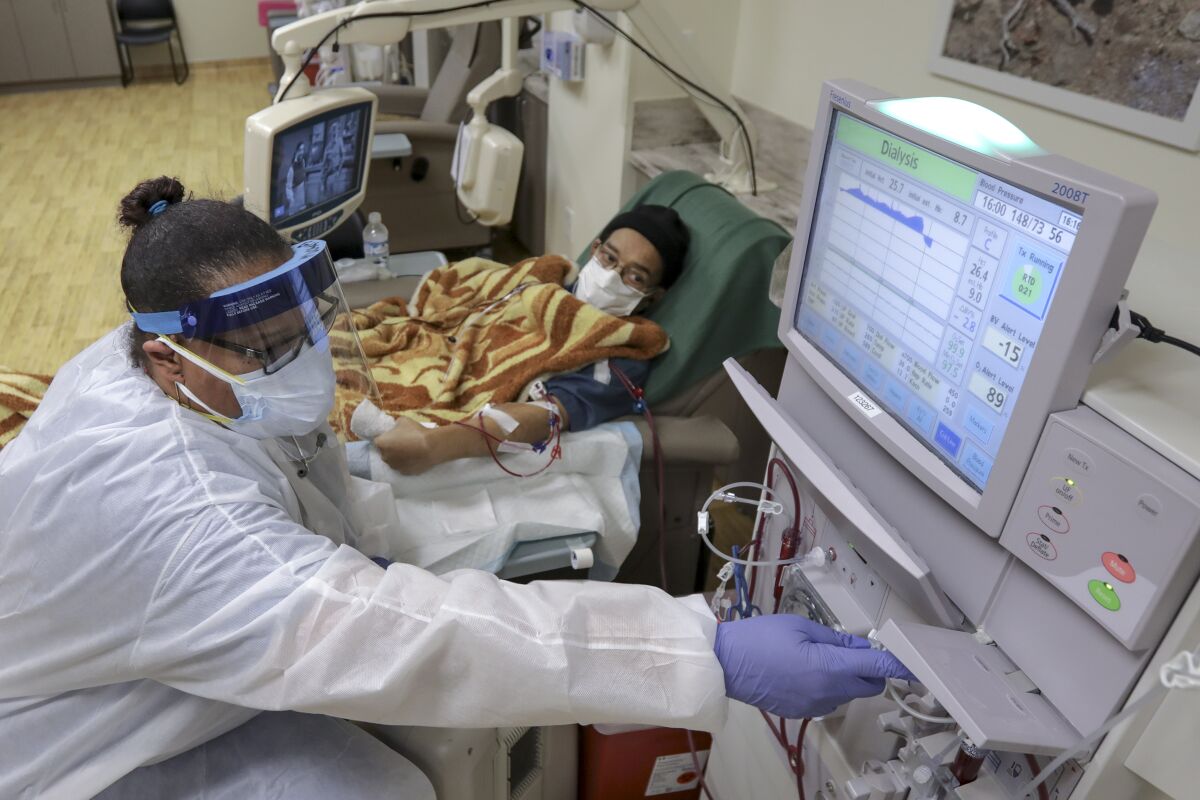 A hemodialysis nurse, left, attends to a COVID-19 patient 