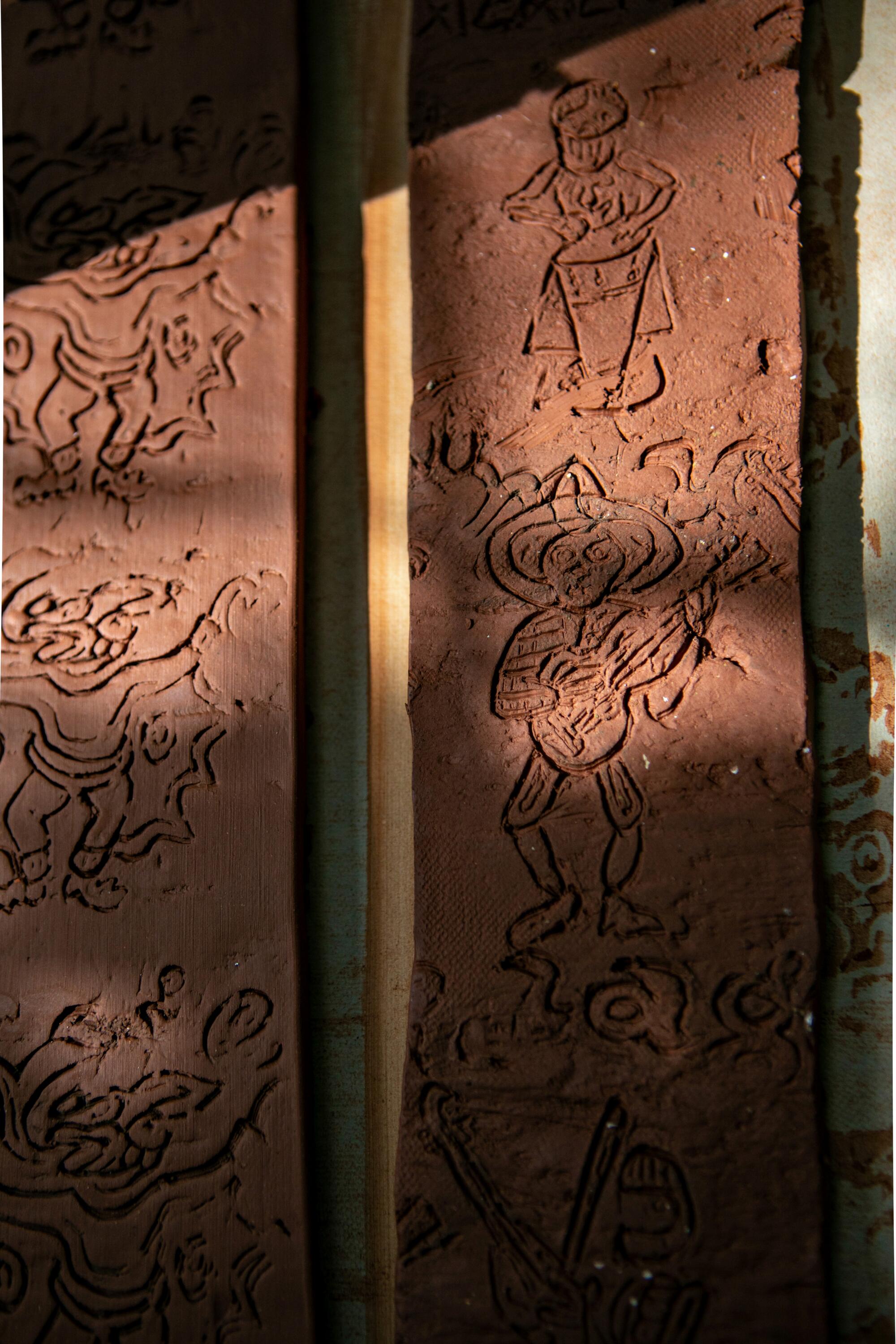 Detail of clay strips with line drawings of characters carved into them.
