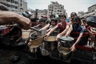 Children reach out empty pans to receive food.
