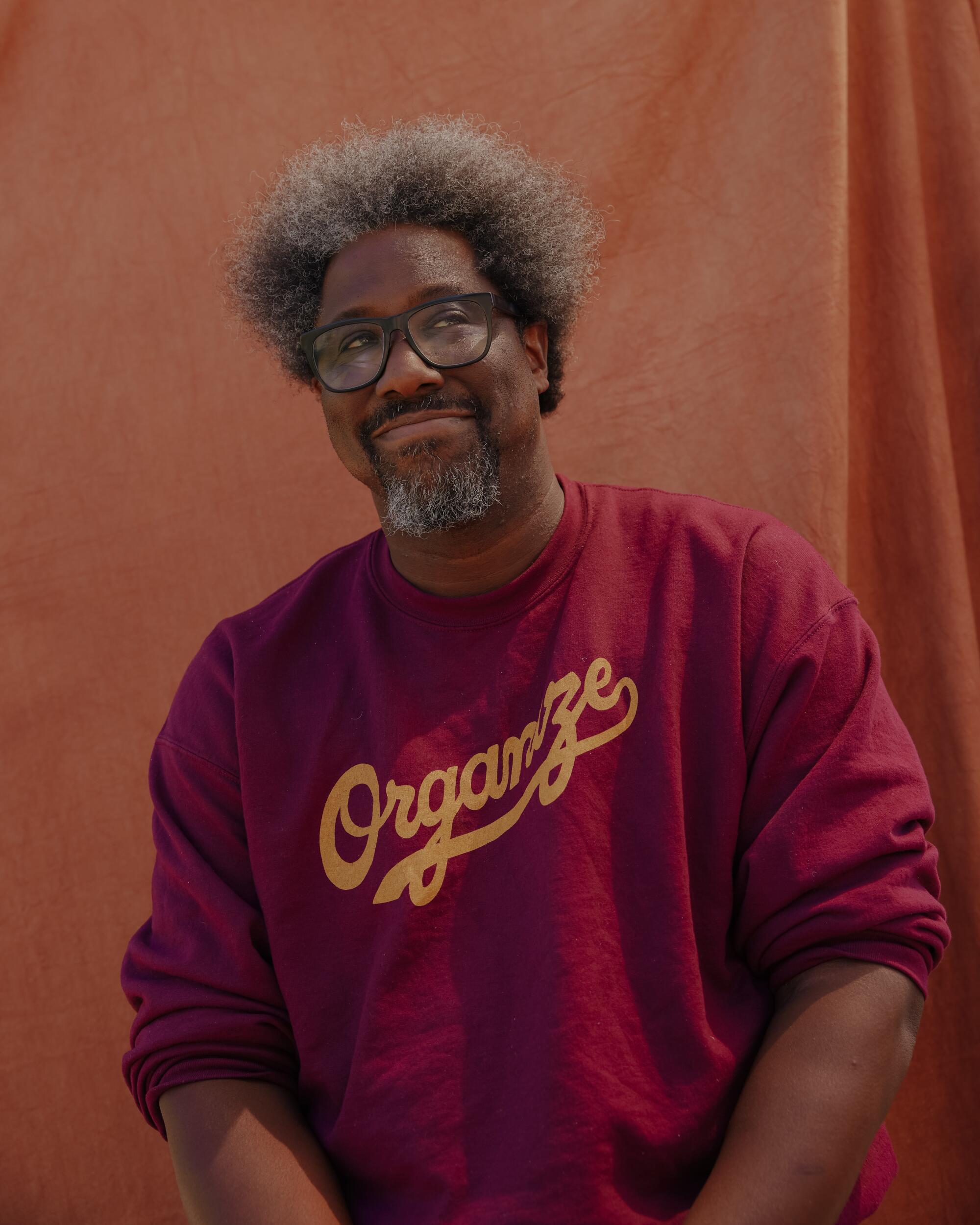 A man in a red sweater in front of an orange fabric background