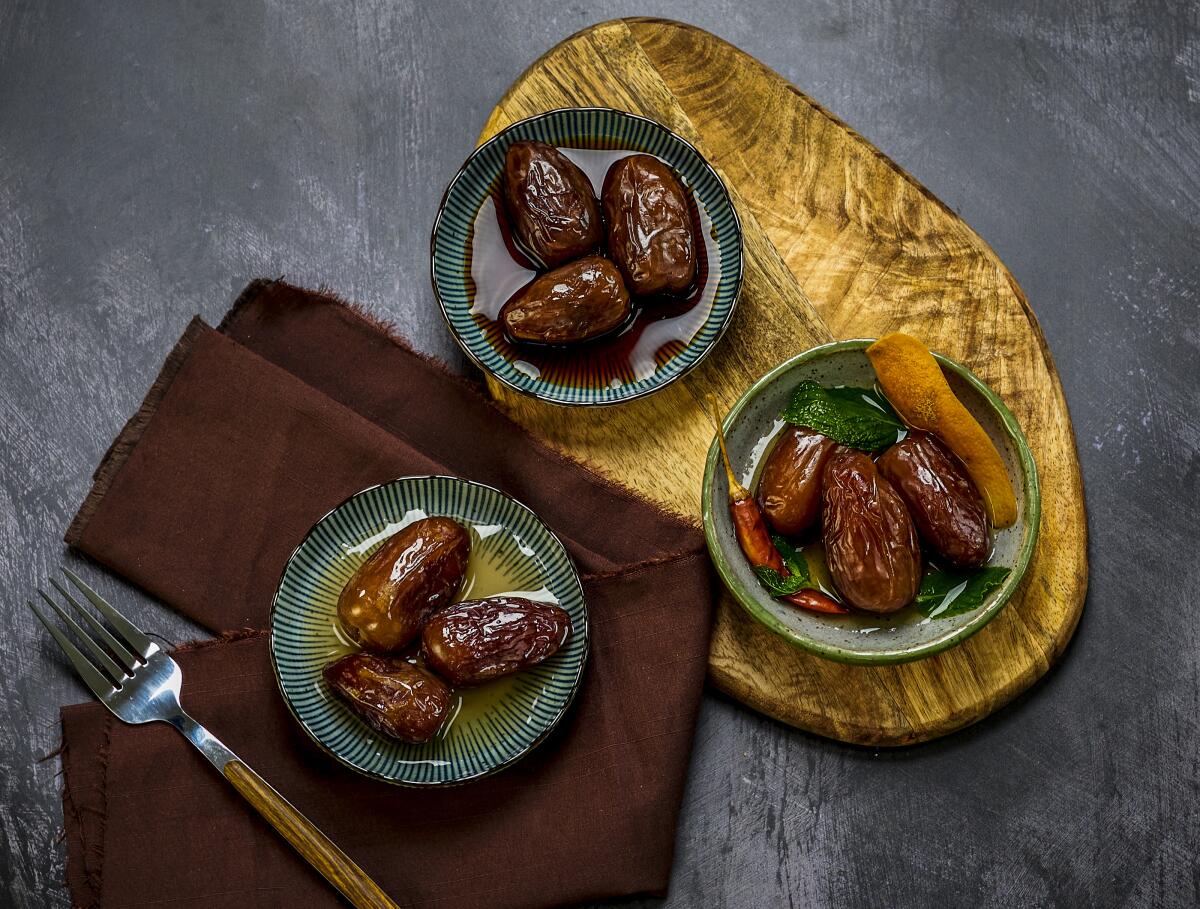 Three dishes of dates in oil, with one a napkin and two on a wooden board