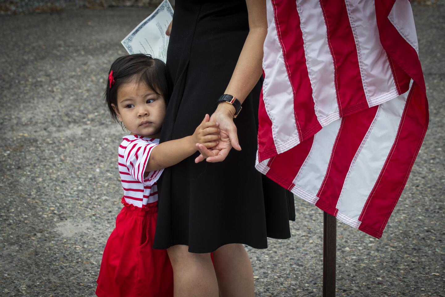 LAGUNA NIGUEL, CA - JUNE 23: Talia Han, 1, hugs her mom, Thao Pham, who's a pop singer with a stage name of Thanh Thao, after taking the oath of allegiance at a drive through citizenship naturalization at the Chet Holifield Federal Building parking lot Tuesday, June 23, 2020 in Laguna Niguel. Pham immigrated to Westminster from Vietnam. About 210-270 people a day have appointments throughout the day for 11 days in seven locations across Southern California. Due to the COVID-19 pandemic, the courts have delegated the authority to U.S. Citizenship and Immigration Services to administer the Oath of Allegiance at the naturalization ceremony. Taking the oath completes the process of becoming a U.S. citizen. (Allen J. Schaben / Los Angeles Times)