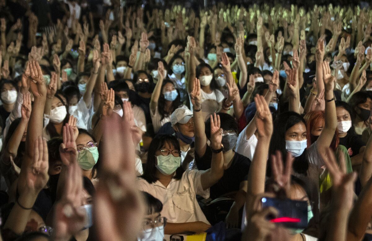 Masked students in Thailand raise three fingers in a salute