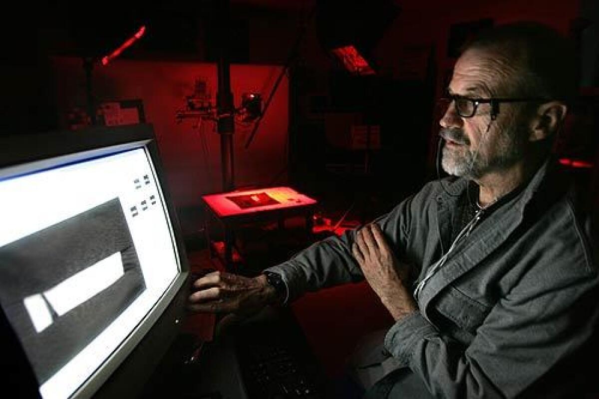 Megavision President Ken Boydston looks at a computer screen as LEDs in the background, emitting red light, illuminate a shard from the 10th century BC with the oldest Hebrew text ever discovered.