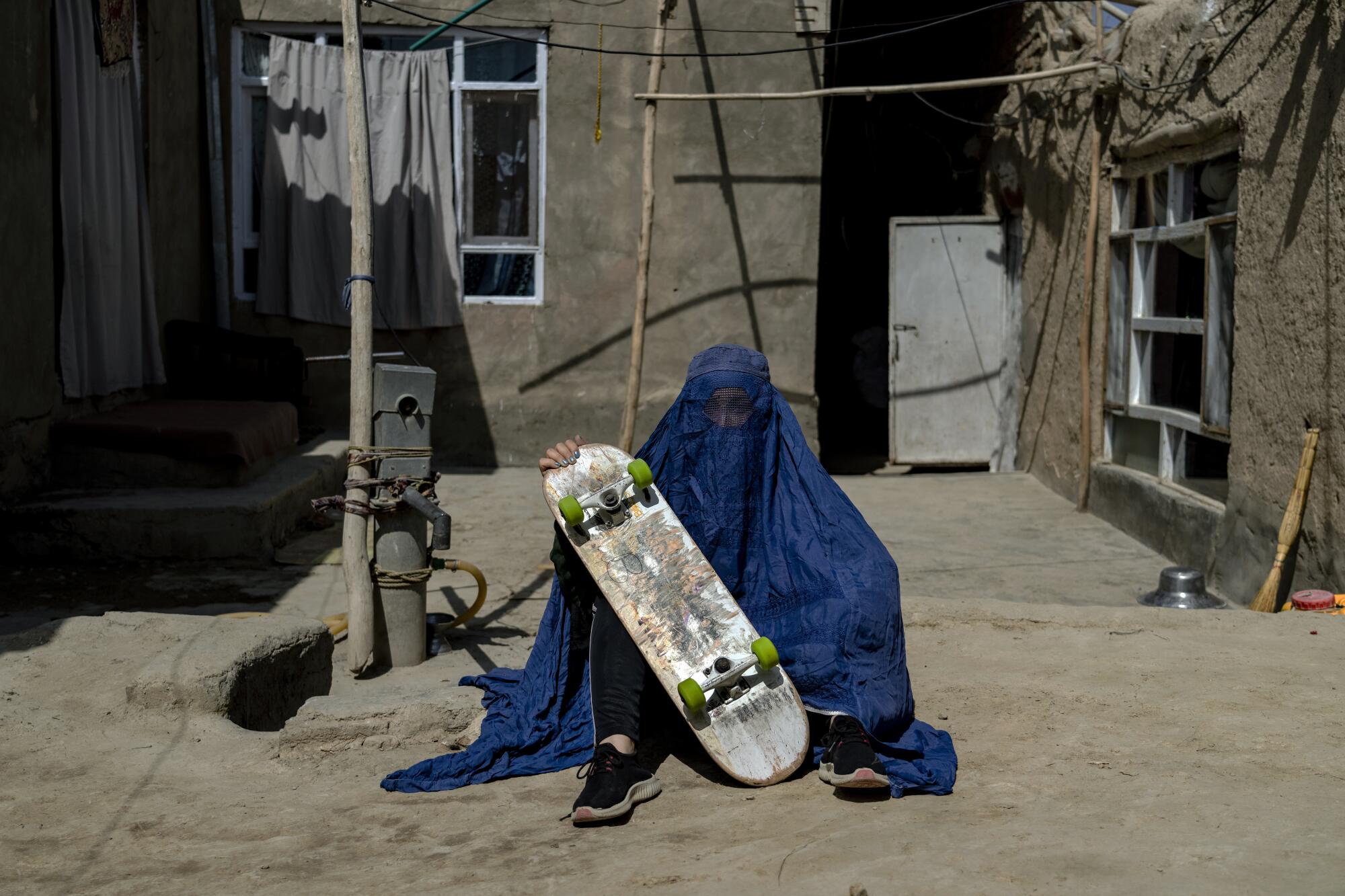 An Afghan girl in a burqa poses with her skateboard.