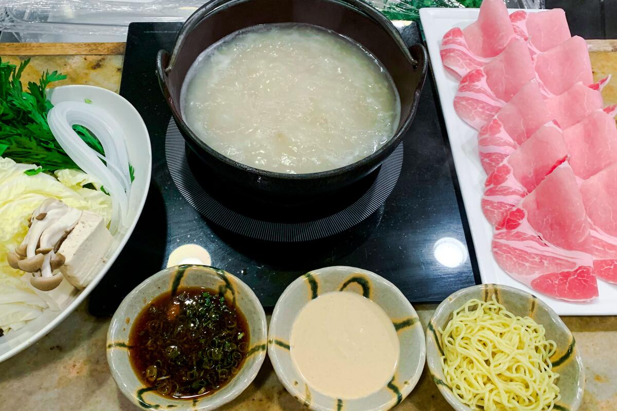 A black pot of broth with sliced raw meat and dishes of sauce and noodles