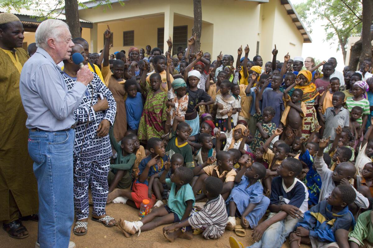 Jimmy Carter speaks into a microphone as a group of youths and adults look on