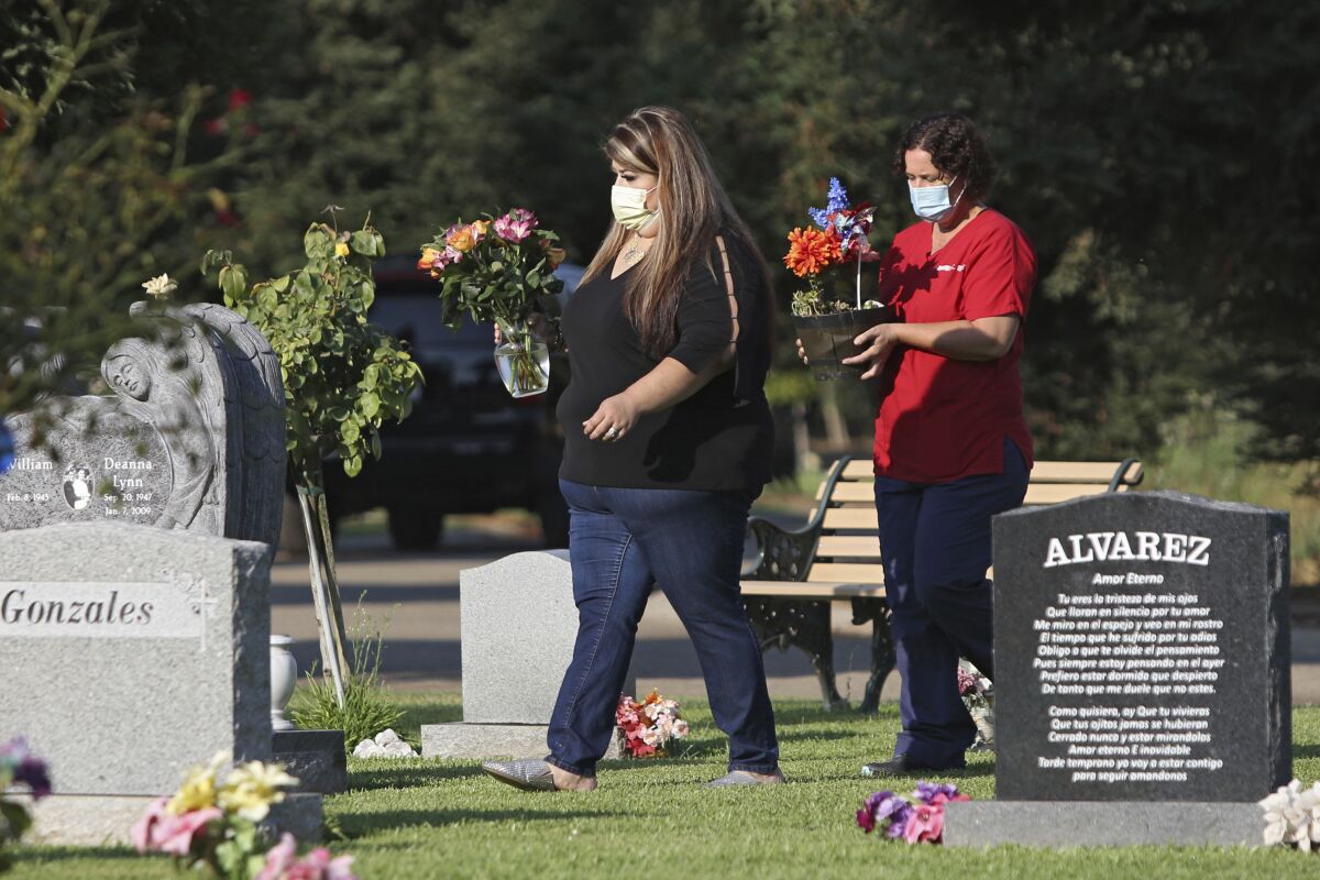 Lori Gonzalez, left, and Rachel Spray carry flowers to the temporary grave marker of Gonzalez's sister and Kaiser Permanente Fresno Medical Center nurse, Sandra Oldfield, at the Sanger Cemetery in Sanger, Calif., Saturday, Aug. 29, 2020. Oldfield died after being exposed to the novel coronavirus. Workers at the hospital said they did not have the proper personal protective equipment. (AP Photo/Gary Kazanjian)