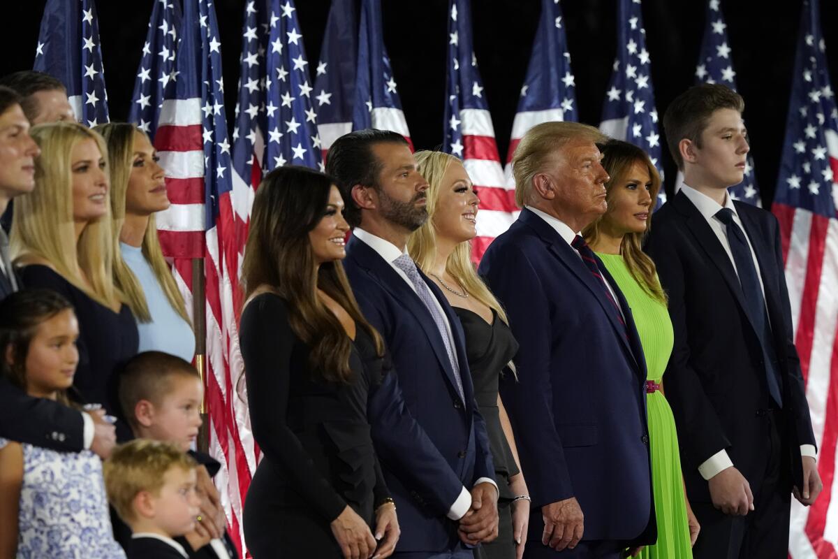A group of people stand in front of a row of American flags.