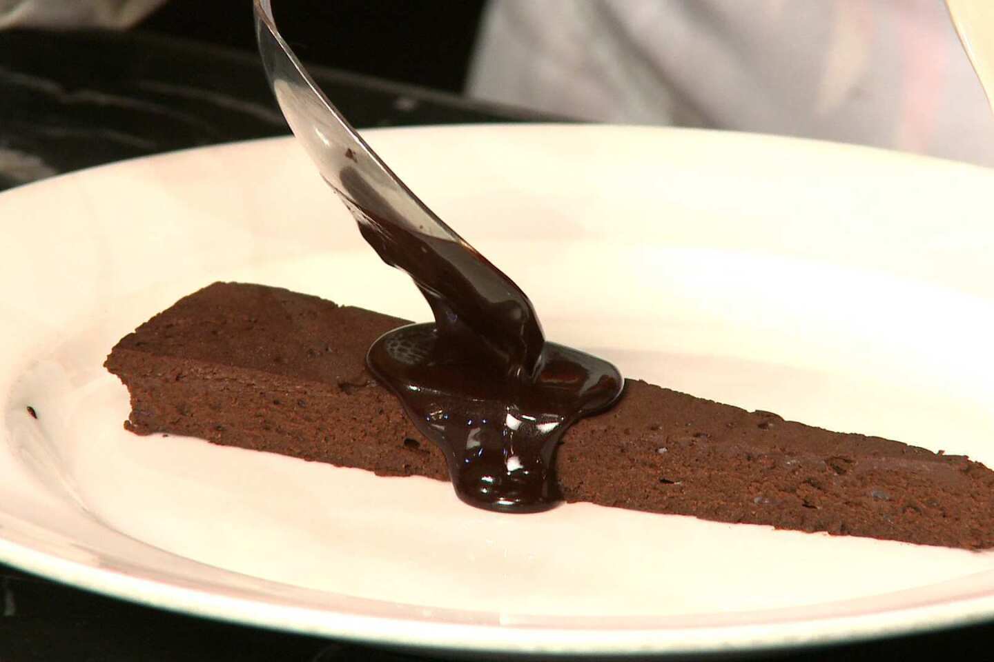 Chef Nancy Silverton spoons warm chocolate onto a slice of chocolate cake. Cake recipe.