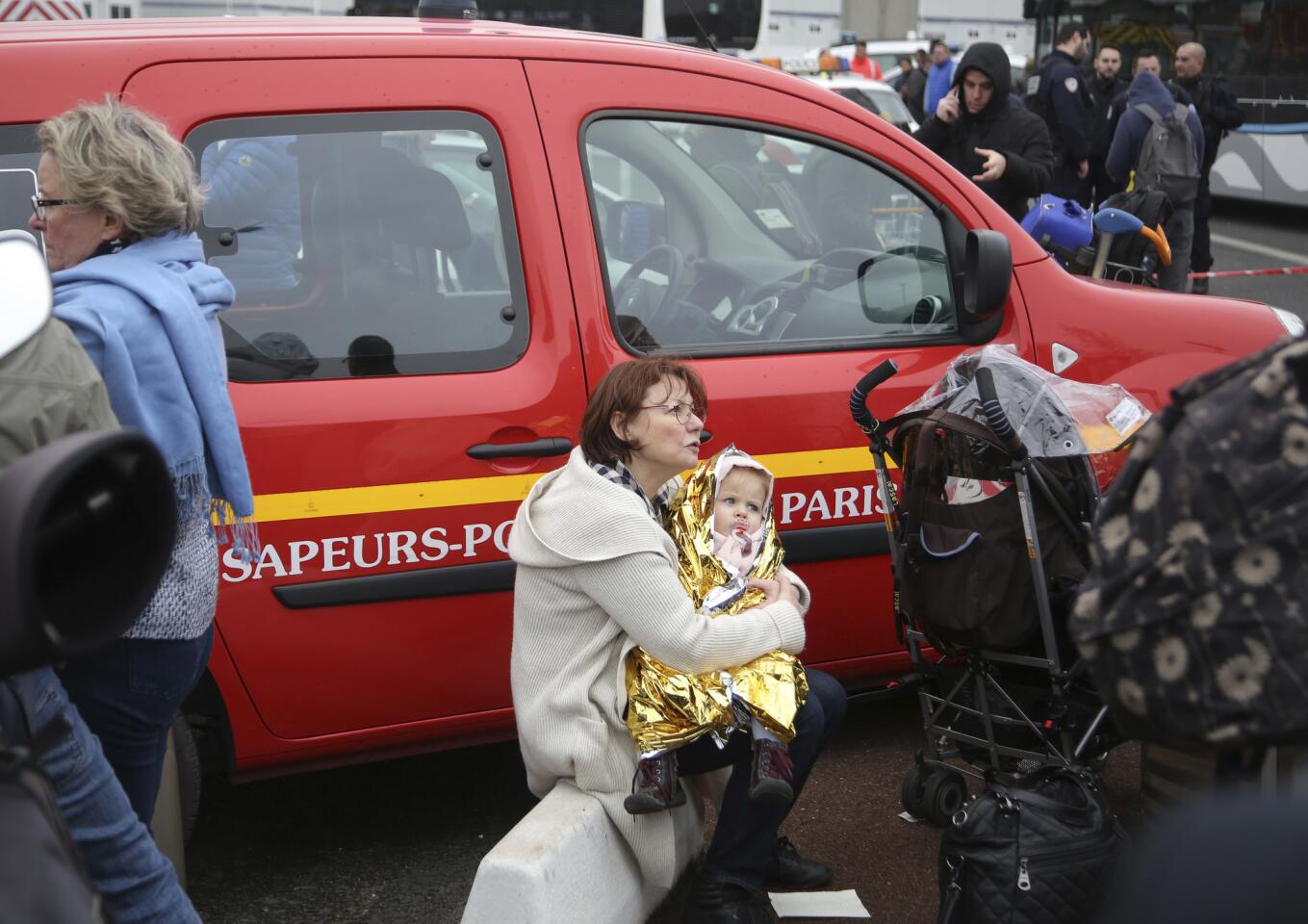 A traveler holds a baby outside Orly airport south of Paris on Saturday after a man was shot by French soldiers.