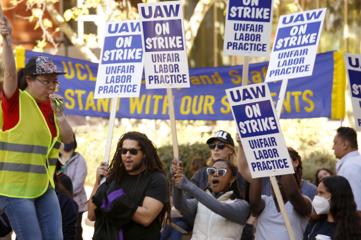 People hold signs reading "UAW On Strike: Unfair Labor Practice."