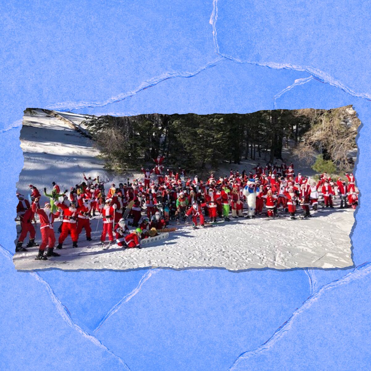 Dozens of people in red suits and white beards wave while standing on a snowy slope.