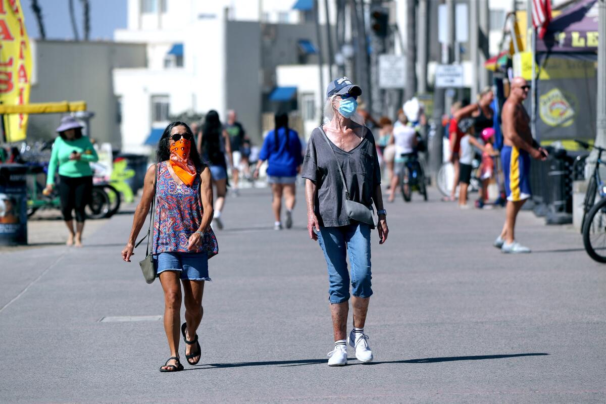 Two women wearing face coverings walk on the boardwalk in Huntington Beach on Oct. 16.