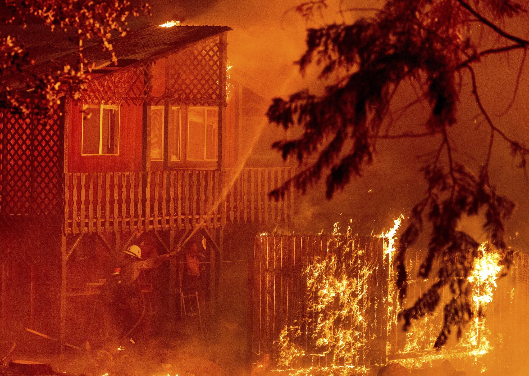 Firefighters work to save a home as the Dixie fire tears through the Indian Falls community in Plumas County, Calif.
