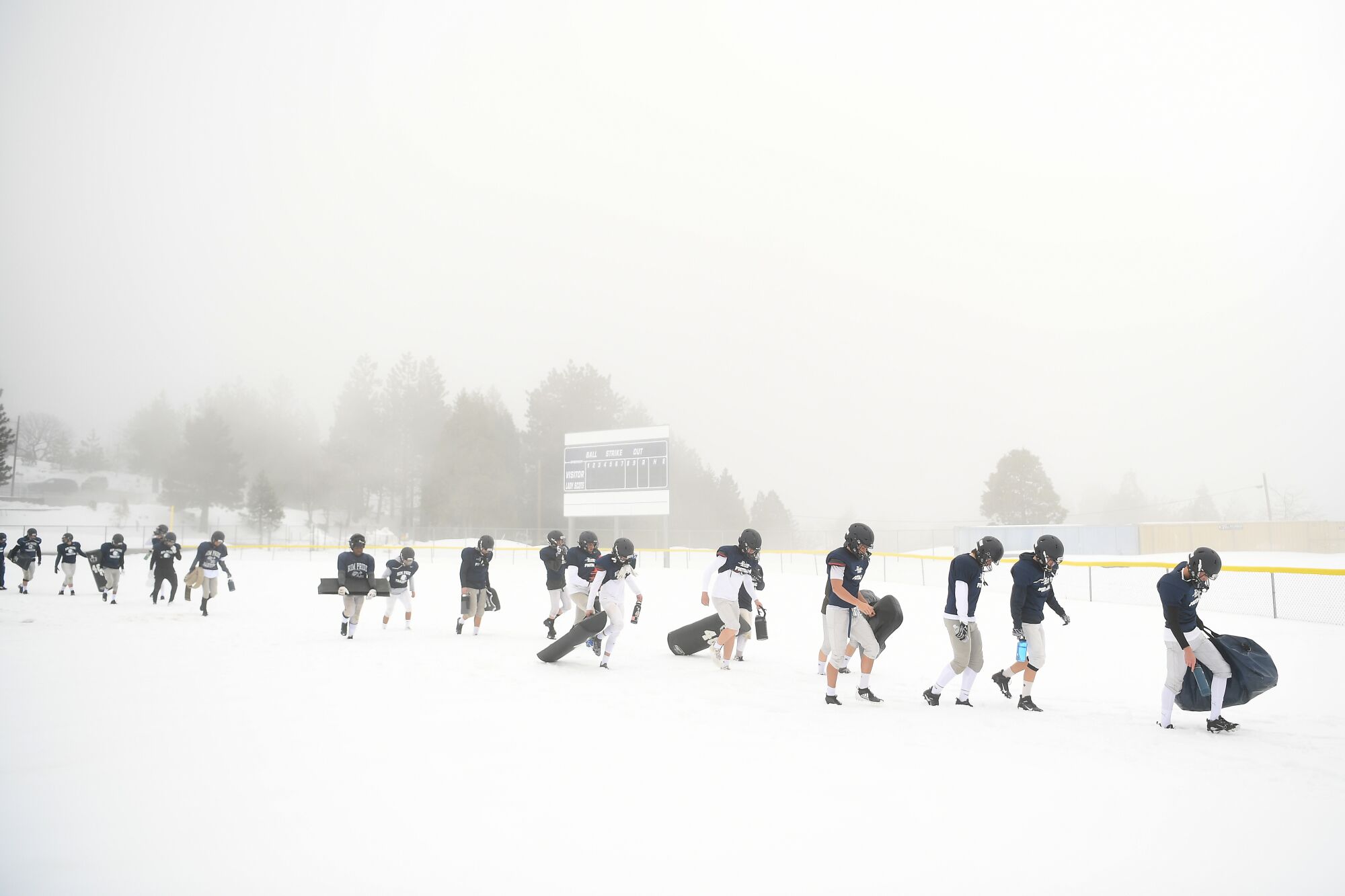 Football players walk to the practice field in snow.