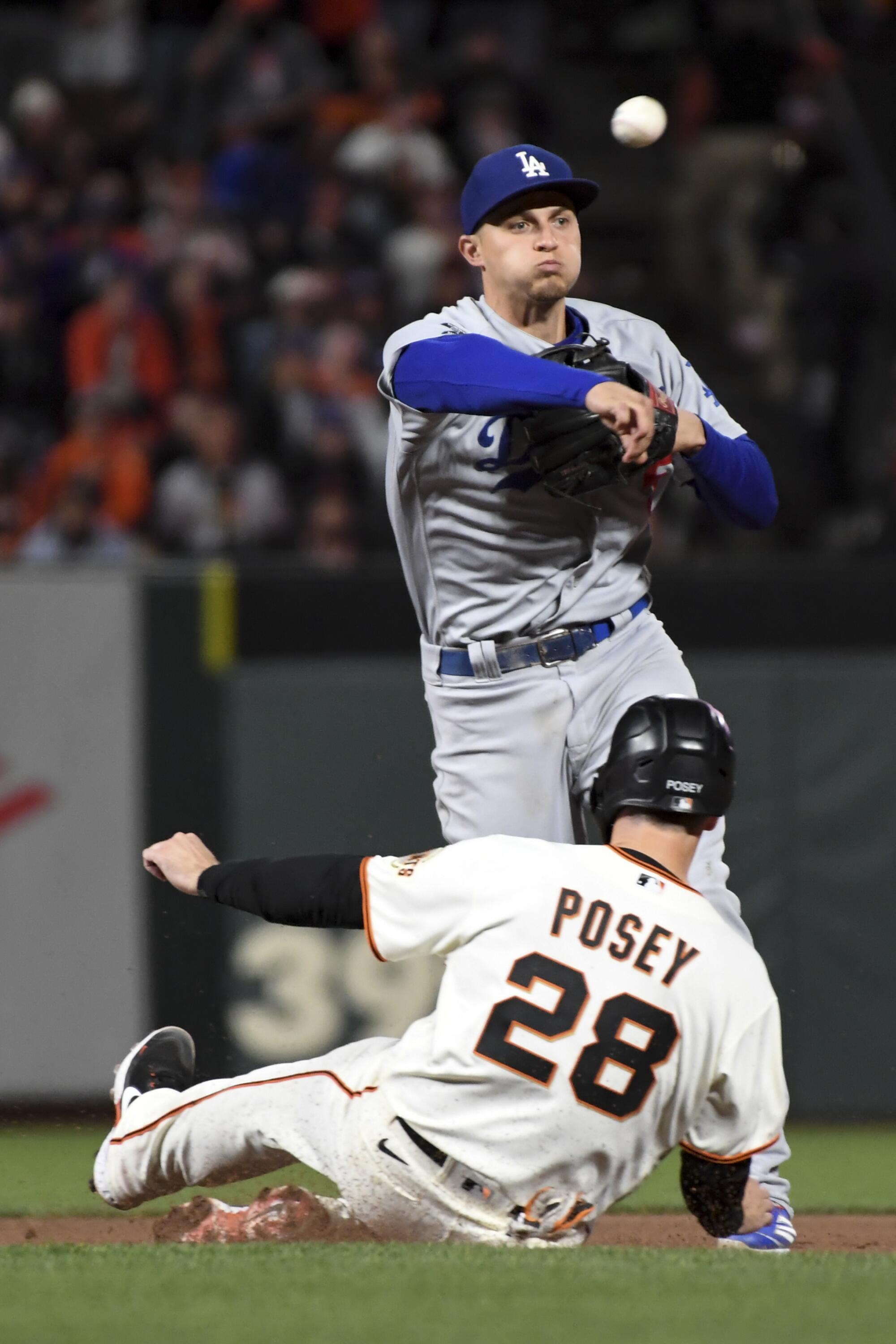 Dodgers shortstop Corey Seager, top, throws to first after forcing out Giants' Buster Posey