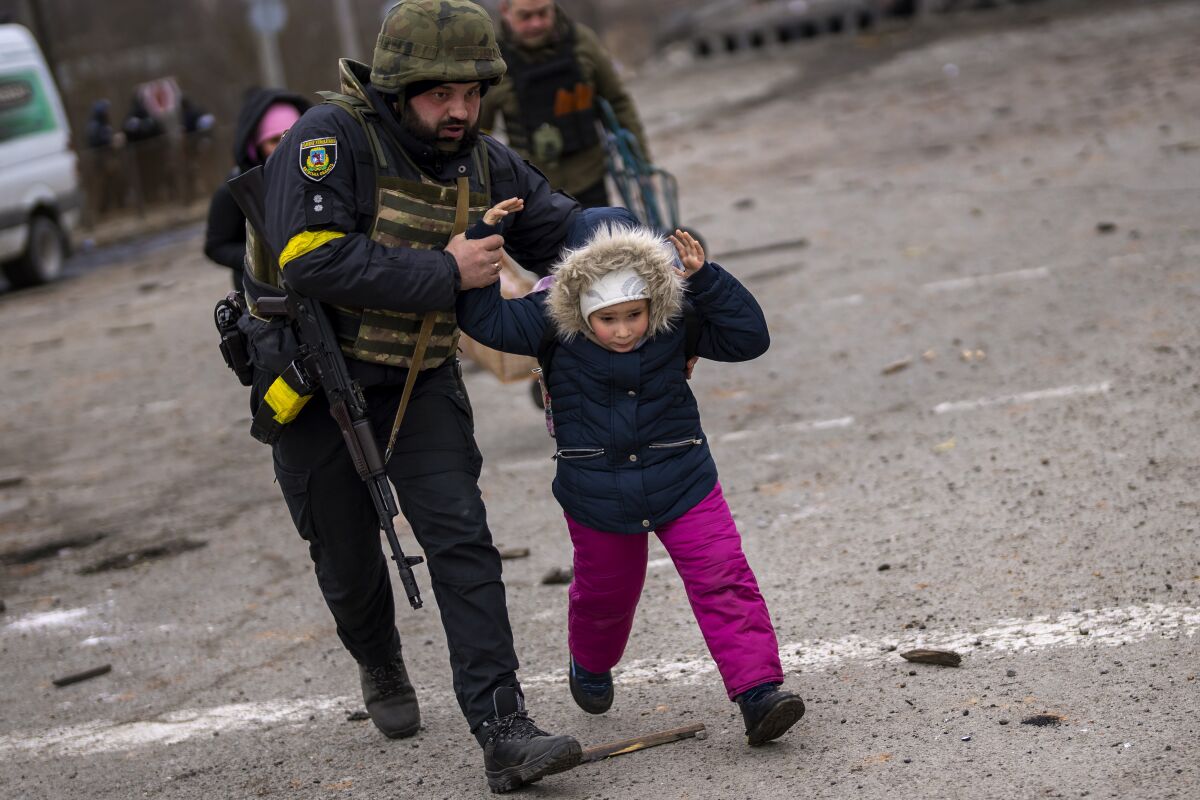 A Ukrainian police officer runs while holding a child as the artillery echoes nearby, while fleeing Irpin on the outskirts of Kyiv, Ukraine, Monday, March 7, 2022. (AP Photo/Emilio Morenatti)