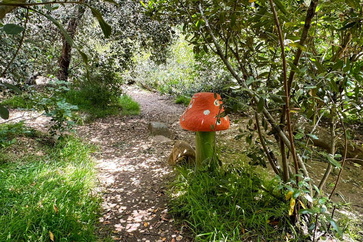 A red statue of a mushroom amid lush greenery in a garden.