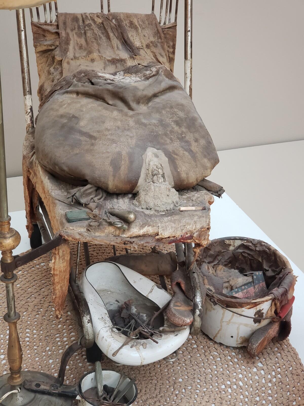 A ruptured bag of cement on a chair surrounded by rags; a soiled bedpan, trash-filled bucket and battered enamel pot.