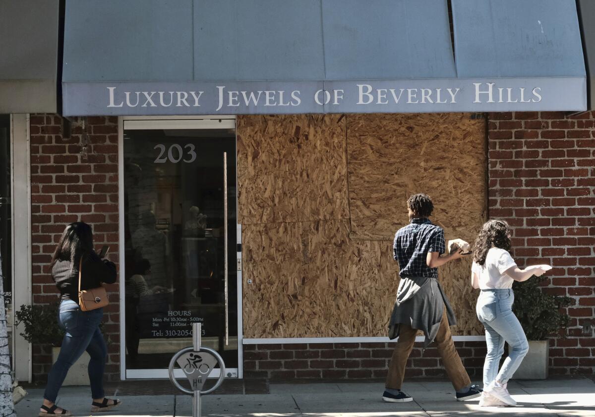 Pedestrians walk past the boarded up Luxury Jewels of Beverly Hills store