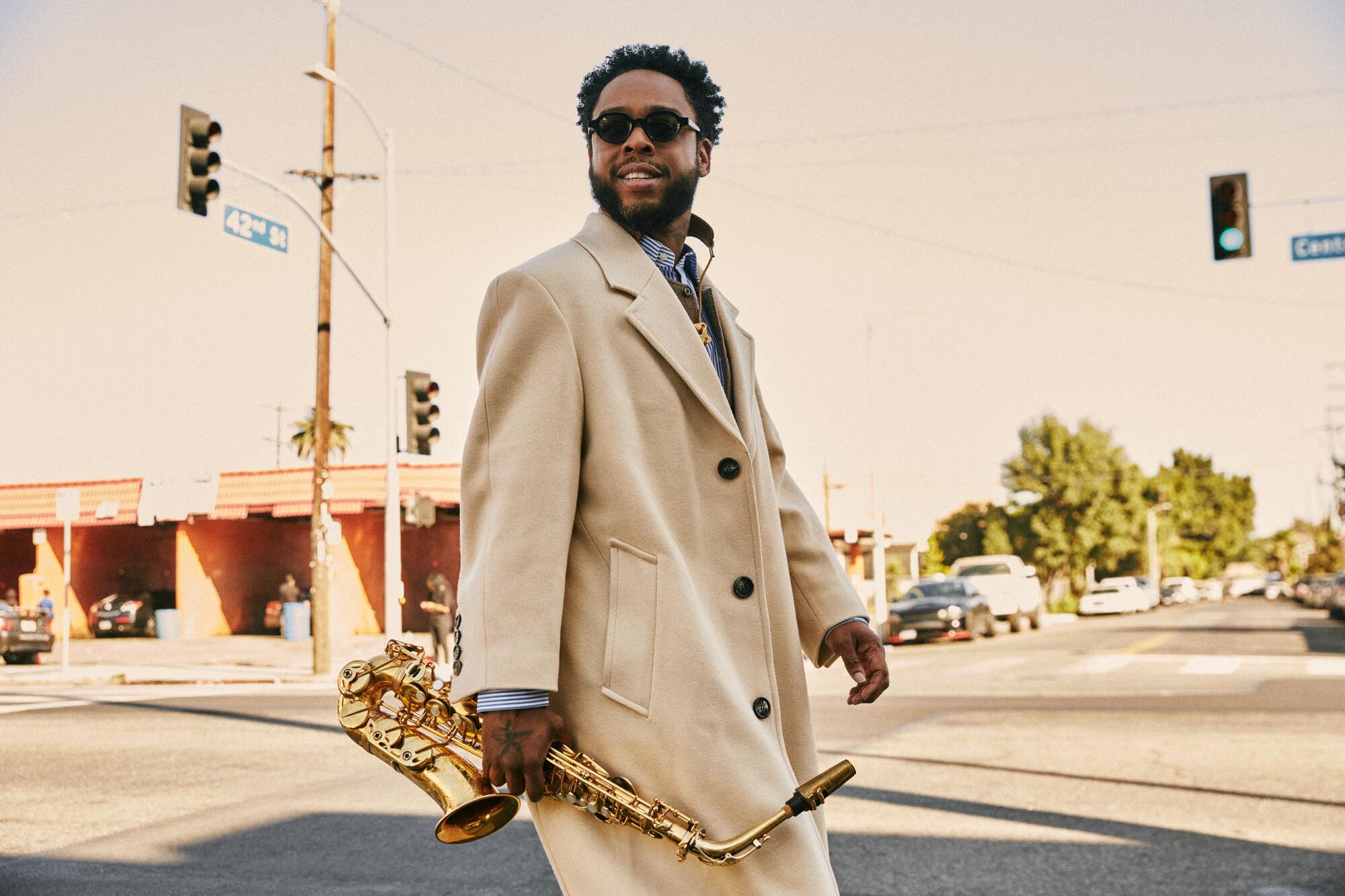 Terrace Martin crosses the street, smiling and carrying a saxophone