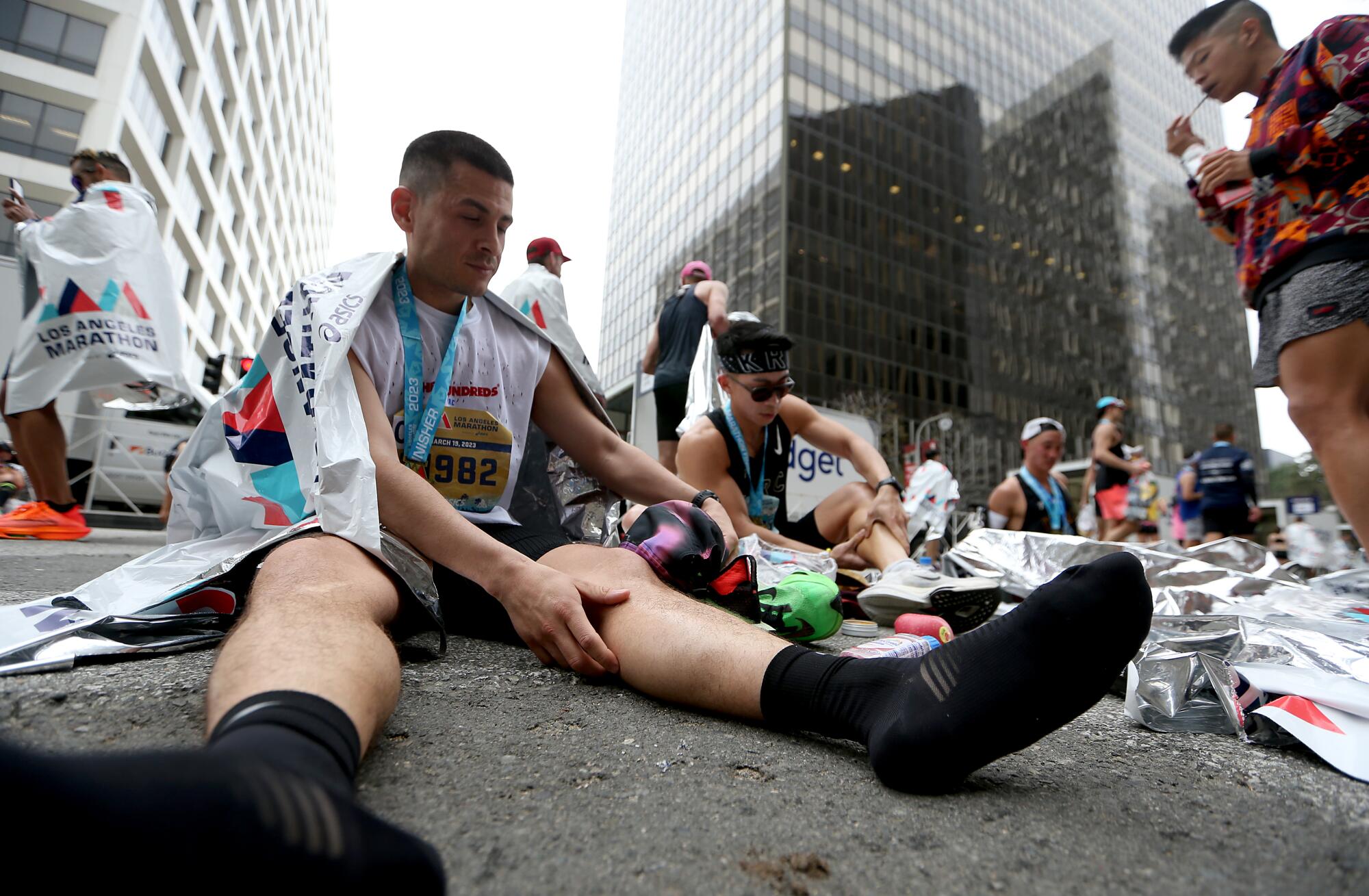 Runners remove their shoes and rest on the streets of Century City after crossing the finish line.