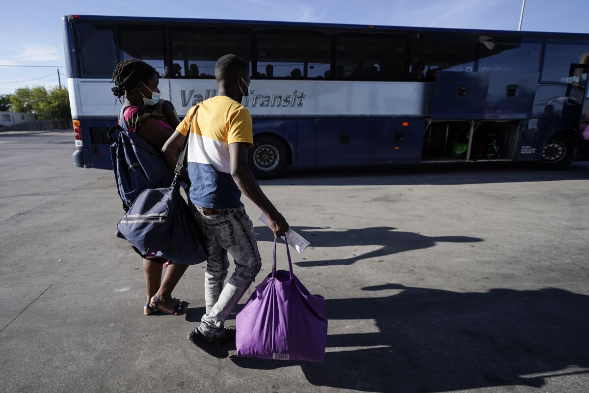 Haitian migrants carrying large bags walk toward a bus 
