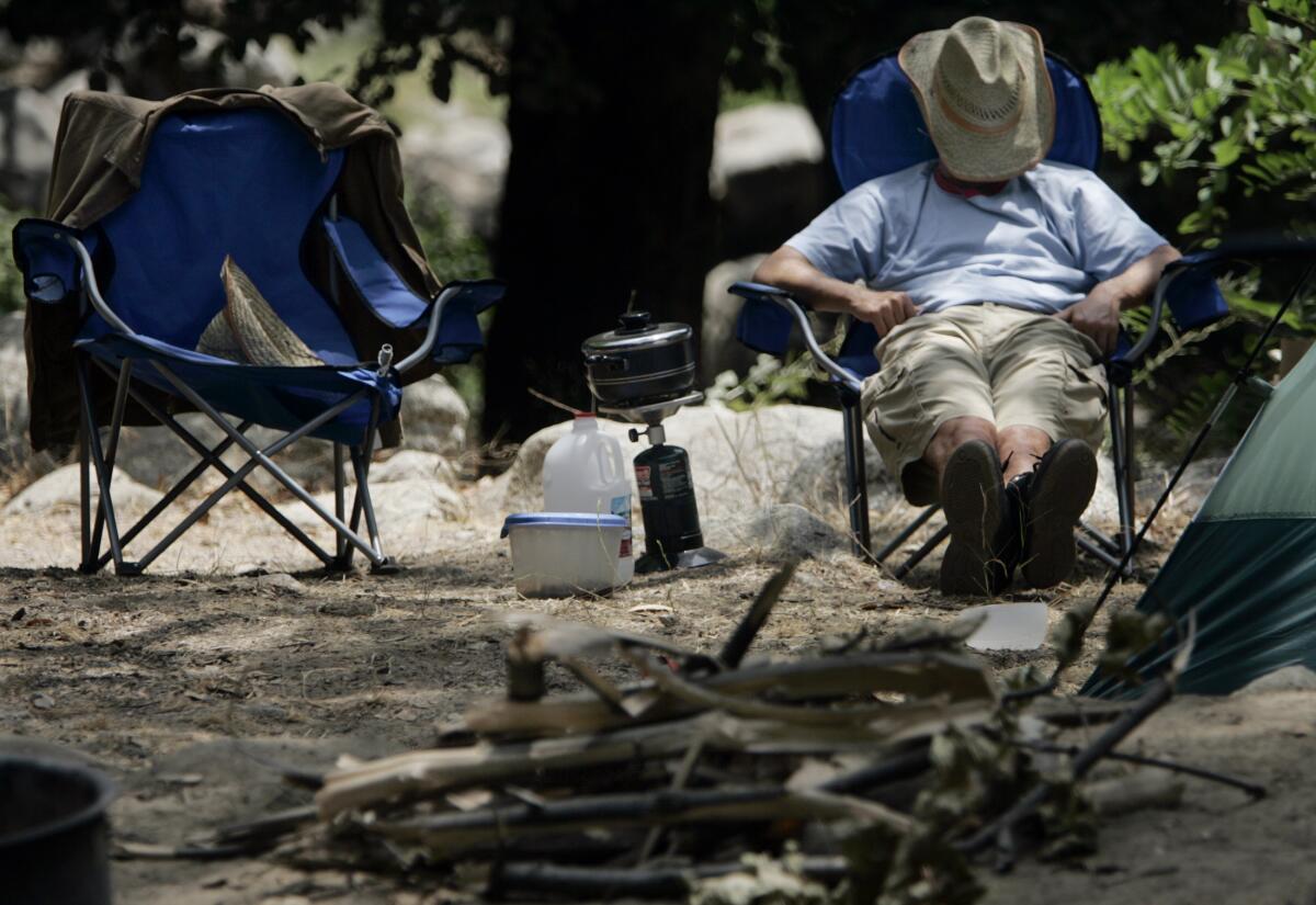 A man in a camping chair rests with his hat over his face. 