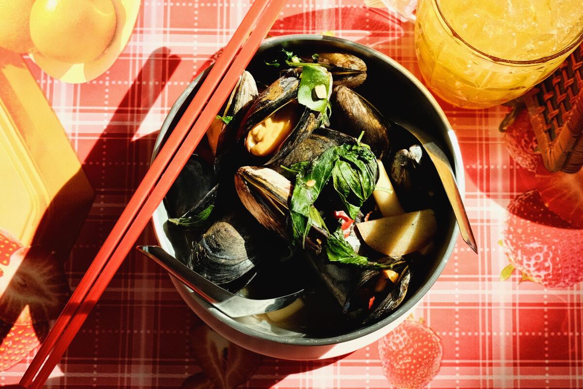 An overhead photo of a bowl of lemongrass mussels with red chopsticks on a red patterned tablecloth at Holy Basil Atwater
