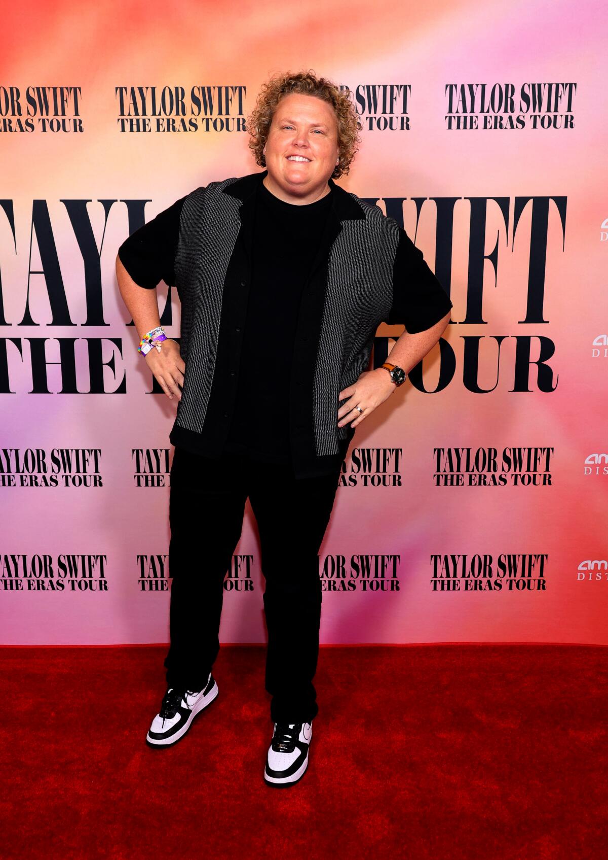 Fortune Feimster poses hands on hips in black pants, sneakers, a gray-and-black top and beaded bracelets